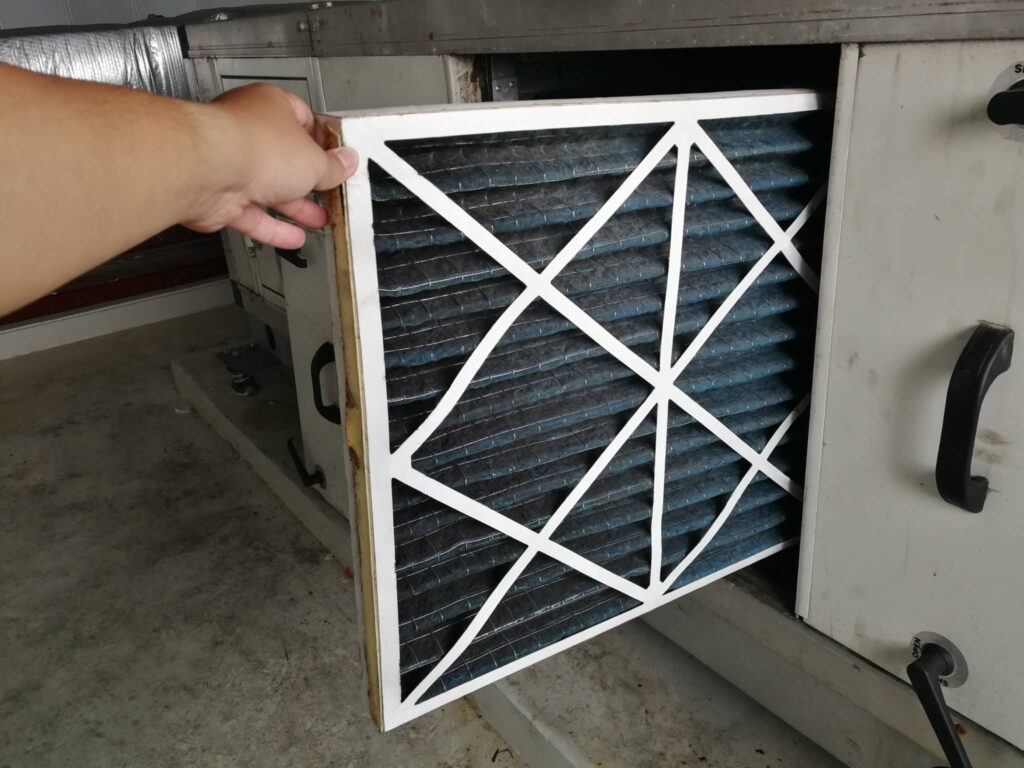 A person is removing a dirty air filter from an HVAC unit for maintenance.