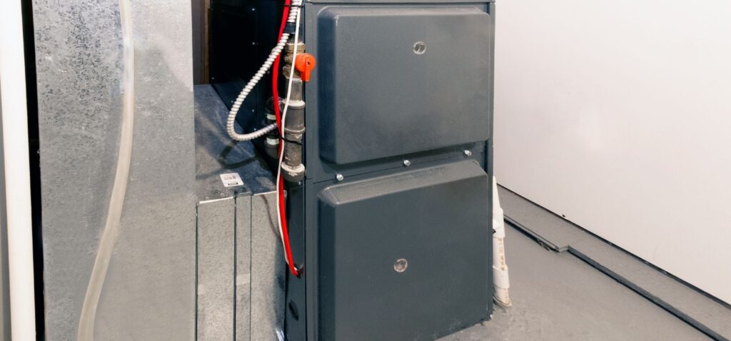 A residential gas furnace installed in a utility room, showing the metal cabinet, ductwork, gas line, and electrical connections.